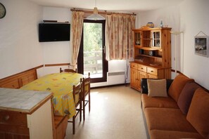 Ein gemütlicher Wohnbereich mit Esstisch, Holzstühlen, einer Couch, einem Schrank und einem an der Wand befestigten Fernseher.