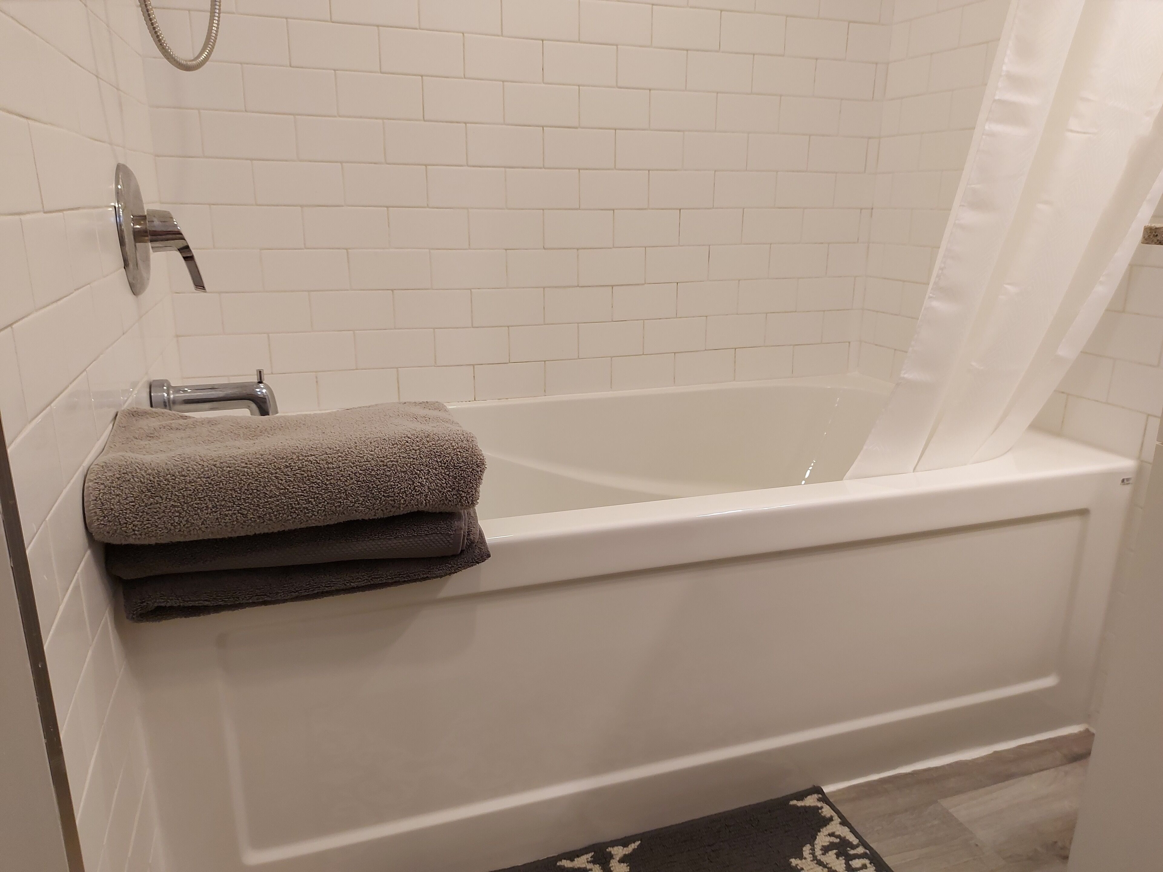 Une salle de bain avec une baignoire blanche, un rideau de douche et un porte-serviettes avec des serviettes pliées.