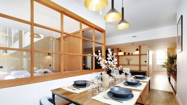 A modern dining area with a long wooden table set for four, large windows, and pendant lighting. - Superb Appartement: 3br/8p - Père Lachaise (Paris)