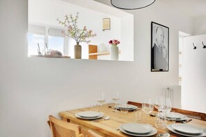 A dining area with a wooden table set for six, white plates, and wine glasses. There are vases with flowers on a shelf above the table. - Amazing Apartment - 6p/2br - Châtelet / Rivoli (Paris)
