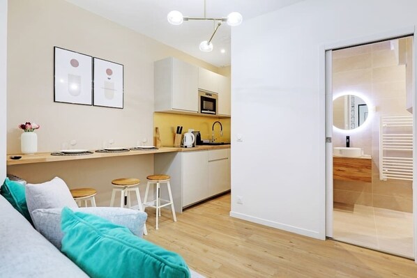 A modern kitchen with white cabinets, a microwave, and a coffee machine. There is a wooden countertop with stools and a vase of flowers. - Charming Appart 4p/1br Le Marais (Paris)