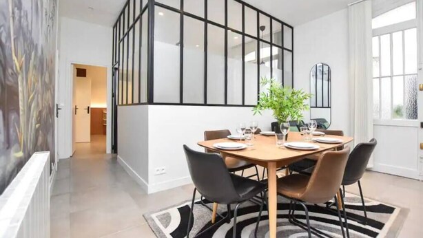 Un espace repas moderne avec une grande table, des chaises noires et une plante en pot.