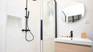 Une salle de bain moderne avec une douche à parois de verre, un meuble-lavabo blanc avec un miroir et un meuble en bois.