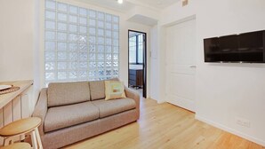 A modern living room with a sofa, a small table, and a TV mounted on the wall. - Charming Appart 4p/1br G Le Marais (Paris)