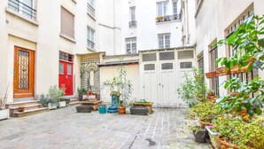 A courtyard with potted plants, a red door, and a white gate.