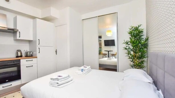 A hotel room with a bed, a small kitchenette, a mirror, and a potted plant.