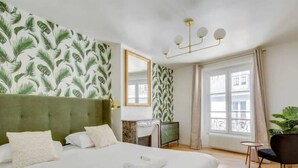 A hotel room with a large bed, a green headboard, a mirror, a dresser, a small table, and a chair. - Amazing Apartment - 8p/3br - Sentier (Paris)