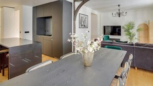A modern kitchen with dark cabinets, a large island, and a dining area with a dark table and chairs. - Amazing Apartment - 8p/3br - Sentier (Paris)