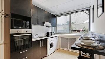 A modern kitchen with dark cabinetry, a built-in oven, microwave, and washing machine. A large window provides natural light and a view of the outside.