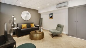 Un salon moderne avec un canapé gris, une table basse ronde, un fauteuil gris et une grande armoire grise.