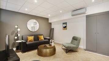 A modern living room with a grey sofa, a round coffee table, a grey armchair, and a large grey wardrobe.