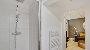 Une salle de bain moderne avec une douche, un radiateur blanc et une vue sur un espace de vie comprenant un canapé et une table basse ronde.