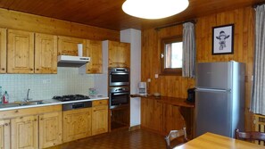 A kitchen with wooden cabinets, a stainless steel refrigerator, and a window with curtains.