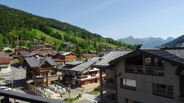 A mountain village with traditional wooden houses, a café, and a view of the surrounding hills.