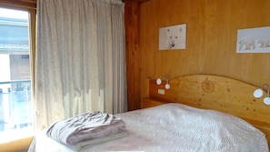 A bedroom with a bed, a wooden headboard, a window with curtains, and wall art.