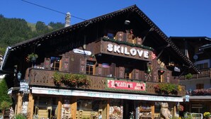 A traditional wooden building with a sign reading "SKILOVE" and "Location de Ski". - Wifi, 150m from resort center, 1st floor, balcony, fireplace or stove, parking, tv, ski locker, 80m² (Les Gets)