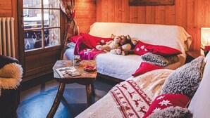 A cozy log cabin interior with a wooden bed, a small table with a glass, and a window with curtains. - Wifi, 150m from resort center, 1st floor, balcony, fireplace or stove, parking, tv, ski locker, 80m² (Les Gets)