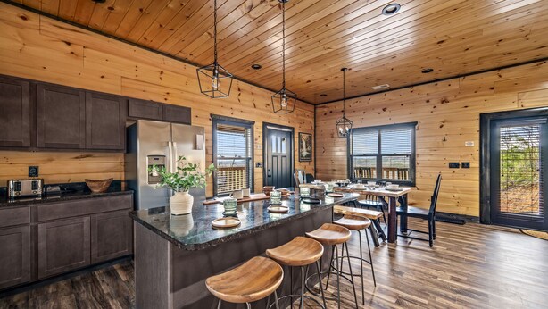 A modern kitchen with wooden walls, a central island with stools, and a dining area with a table and chairs.