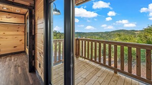 A wooden interior with a large glass door leading to a balcony with a wooden railing.