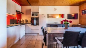 Une cuisine compacte équipée d’un four à micro-ondes, d’un four et d’un réfrigérateur. On y trouve une table à manger avec des chaises et un vase de fleurs.