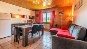 Une pièce chaleureuse avec un plafond en bois, une table à manger avec des chaises, un canapé avec des coussins rouges et une vue sur l’extérieur par une fenêtre.