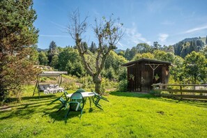 Uma área externa com gramado, com um galpão de madeira, balanço e mesa para piquenique.