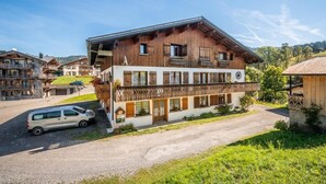 Un immeuble en bois à plusieurs étages, doté de balcons, avec une voiture garée devant et un ciel dégagé.