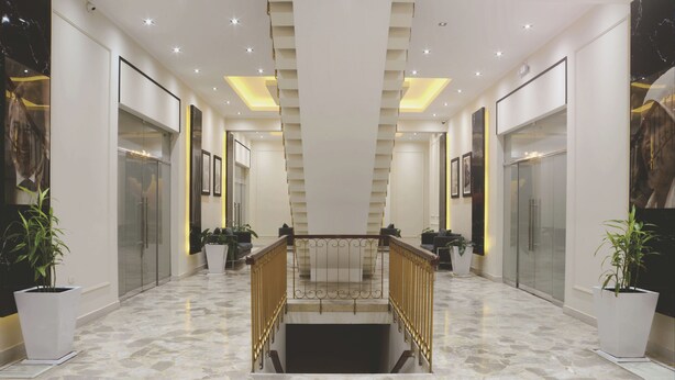 Un moderno vestíbulo de hotel con piso de mármol, una escalera central y plantas en macetas.