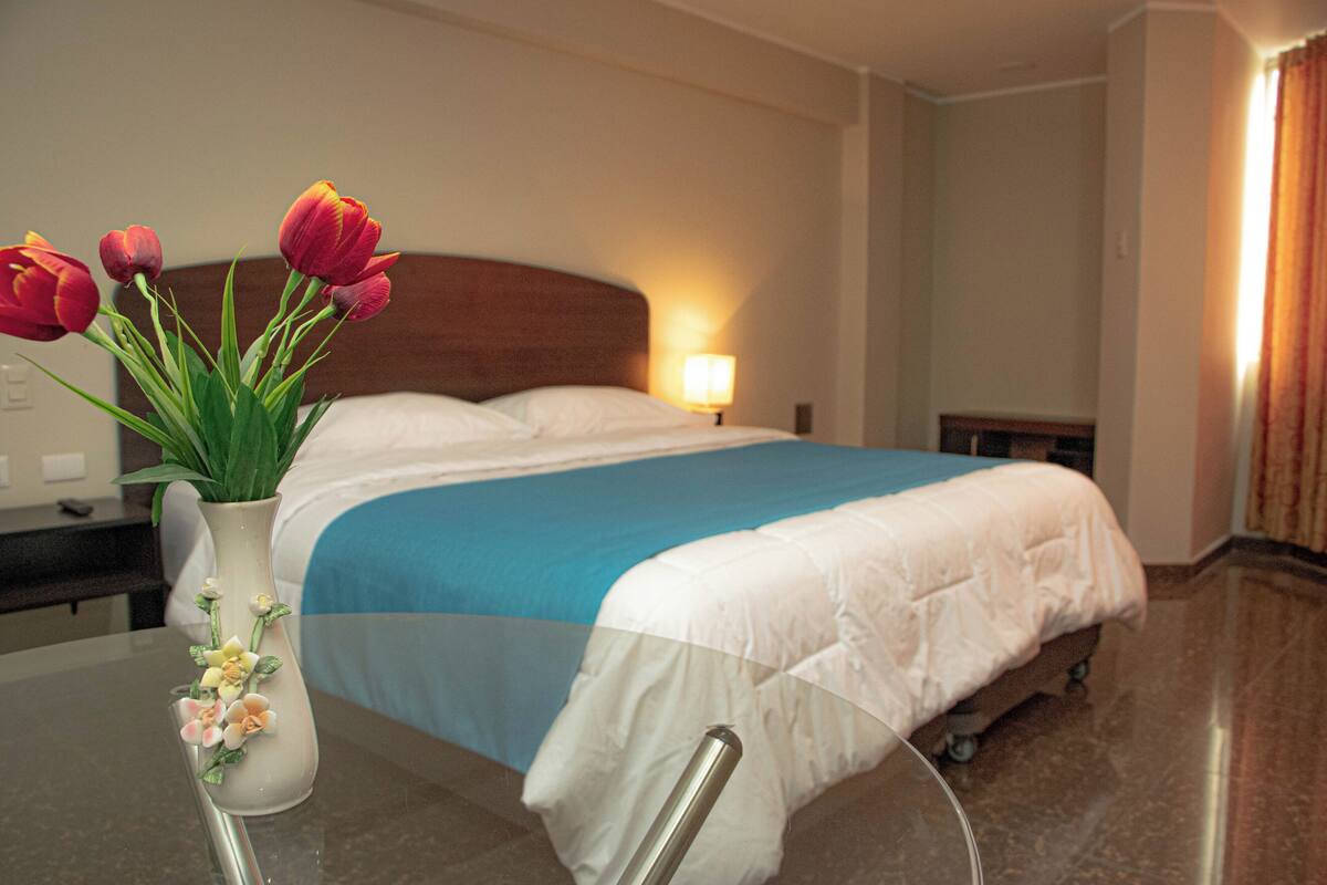 A hotel room with a bed, a nightstand, a lamp, and a vase with flowers.