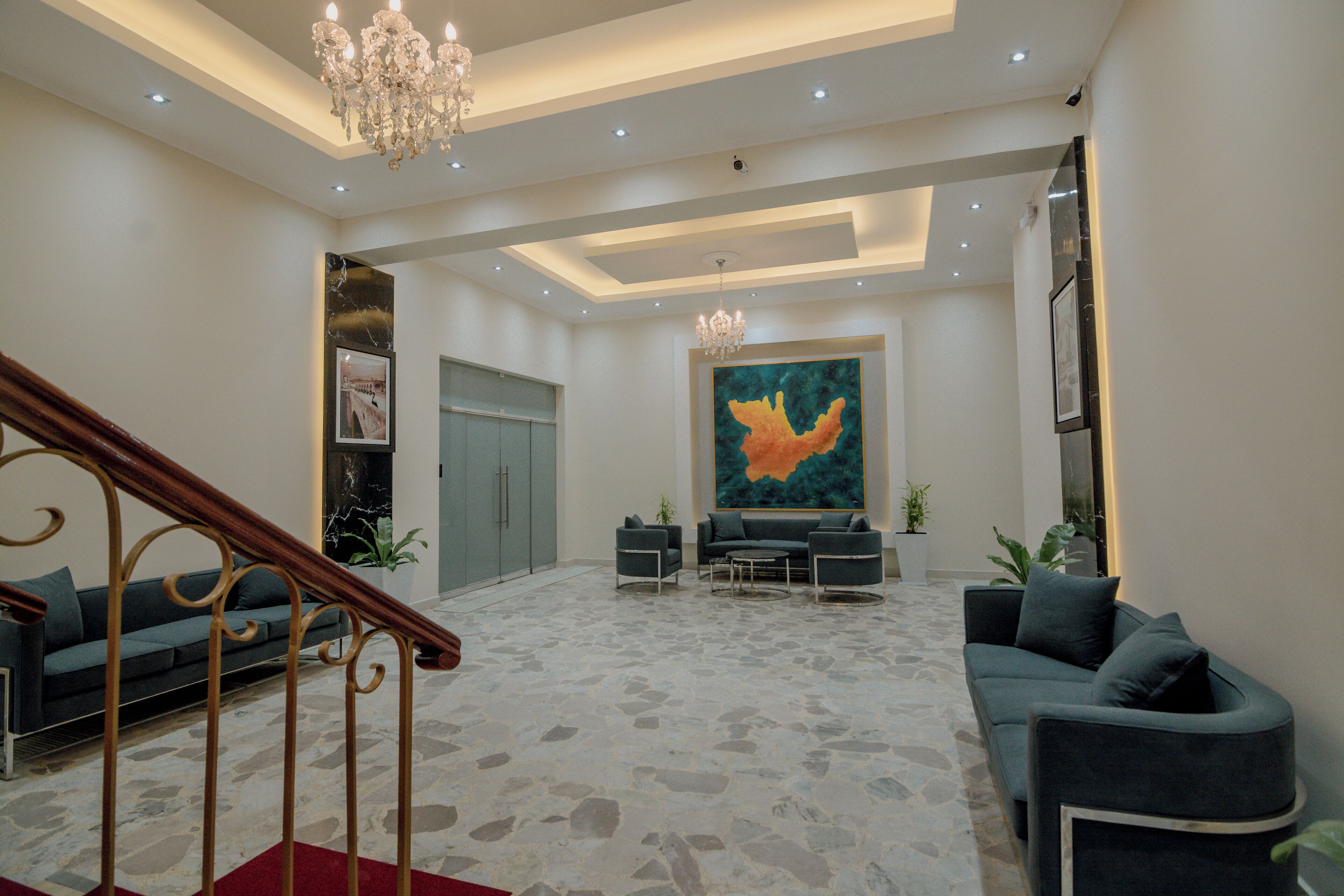 A spacious living area with a staircase, a large abstract painting, and a chandelier.