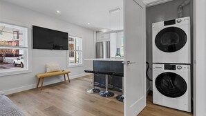A modern laundry room with a washing machine, a bench, and a TV mounted on the wall. - Cambridge/Boston 3BR2Bth Parking, W/D, Subway,A/C (Somerville)