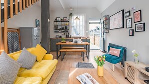 A modern living room with a yellow sofa, a wooden dining table, and a blue armchair. - The Little Cottage, Whitstable (Whitstable)