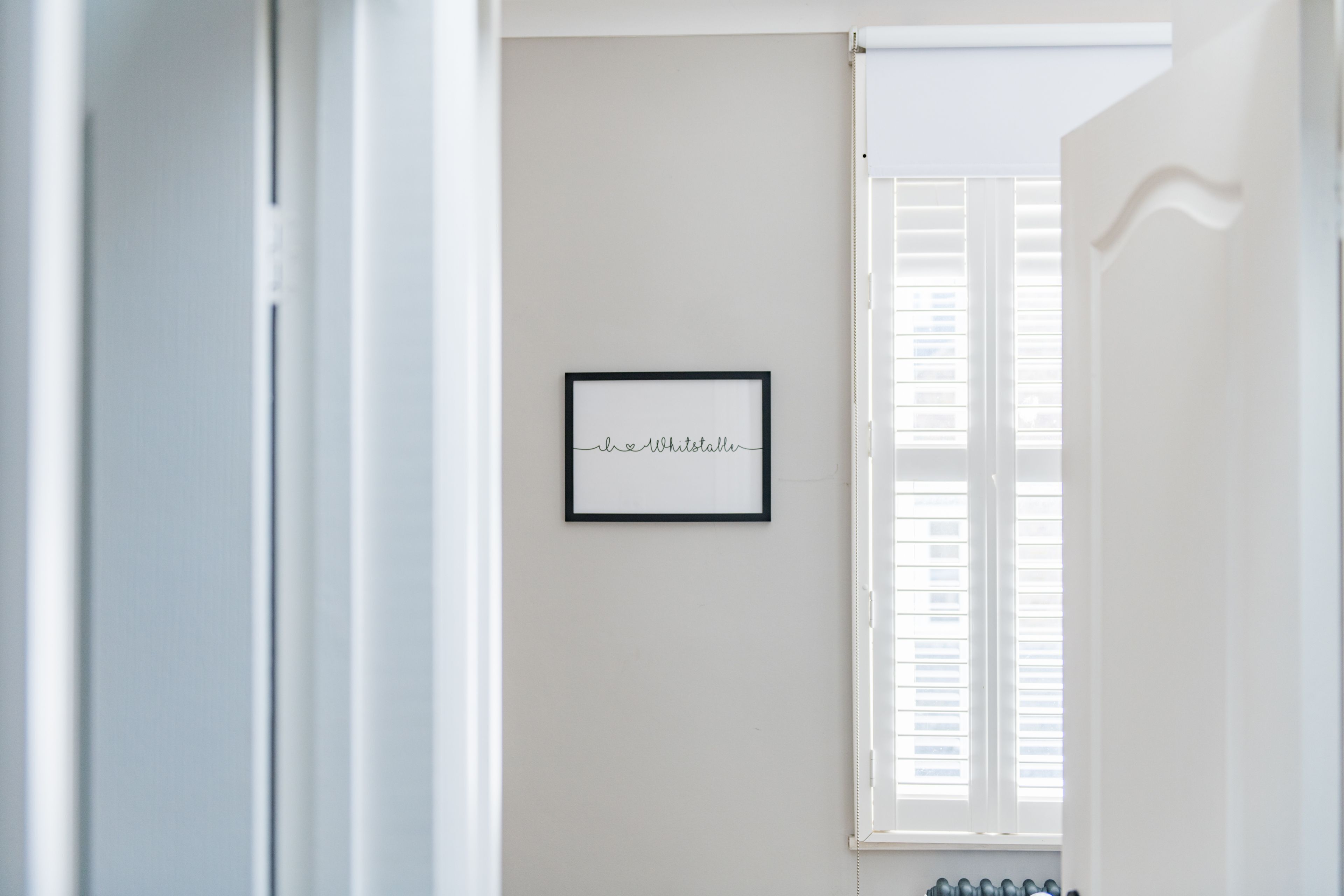 Ein Durchgang zu einem Raum mit einem gerahmten Schild an der Wand und einem Fenster mit Jalousien.
