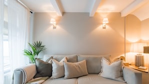 Ein modernes Wohnzimmer mit einem beigefarbenen Sofa, zwei Wandleuchten und einer Topfpflanze.