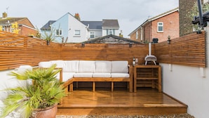 Eine Terrasse mit Holzdeck, einem weißen Sofa und einem Grill.