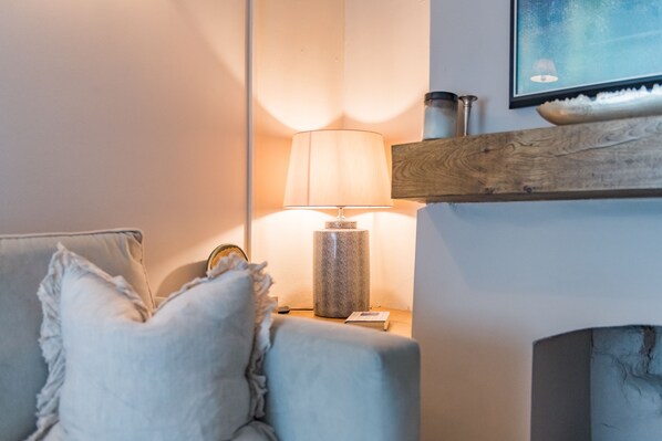 A cozy living room with a sofa, a lamp, a fireplace, and a framed picture on the wall.