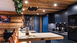 A modern kitchen with dark cabinetry, a wooden dining table, and leather chairs. - PEARL 201 | LES GETS | 14 pers.  | Central (Les Gets)