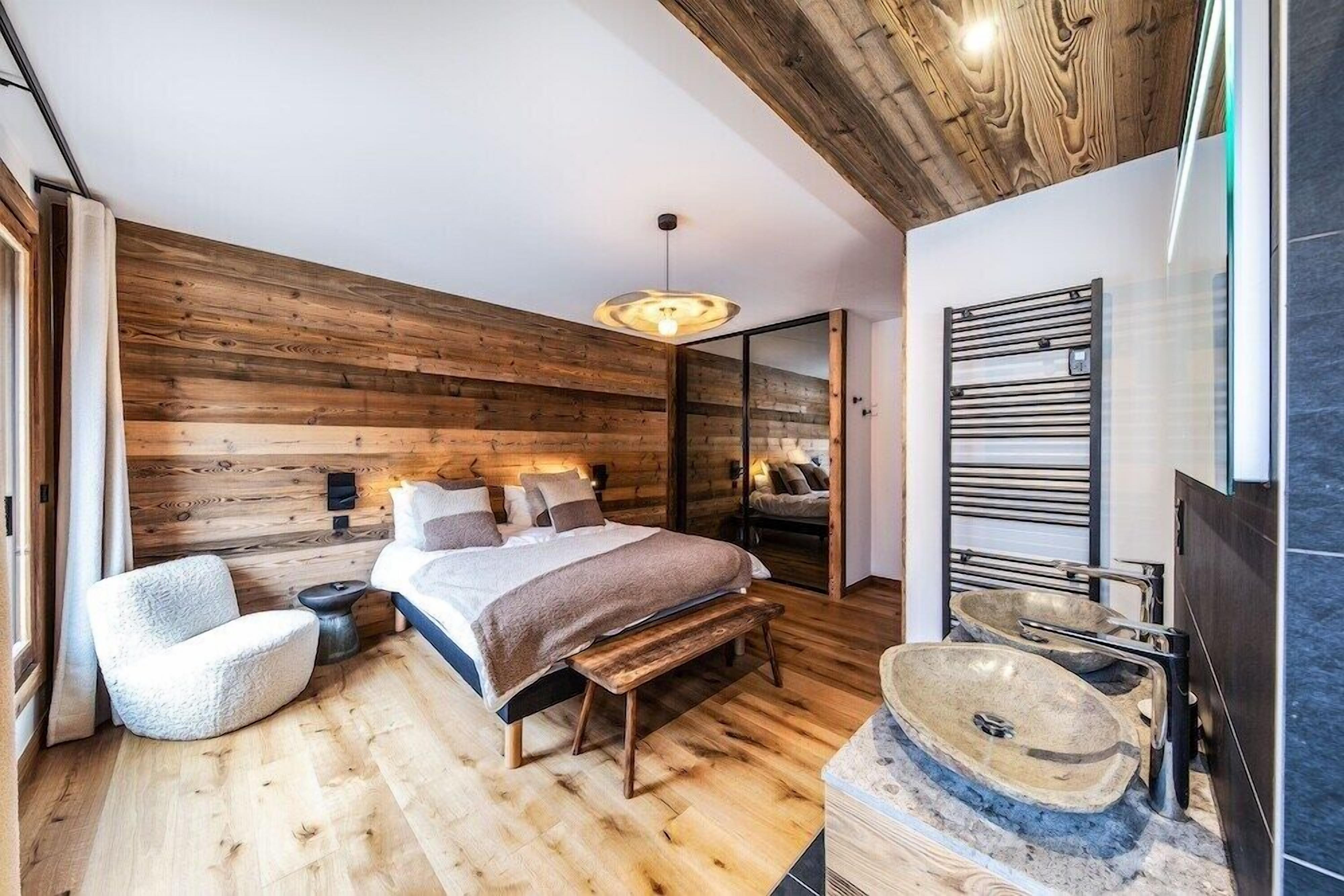 A modern bedroom with a wooden wall, a bed, a bench, a chair, and a large window.