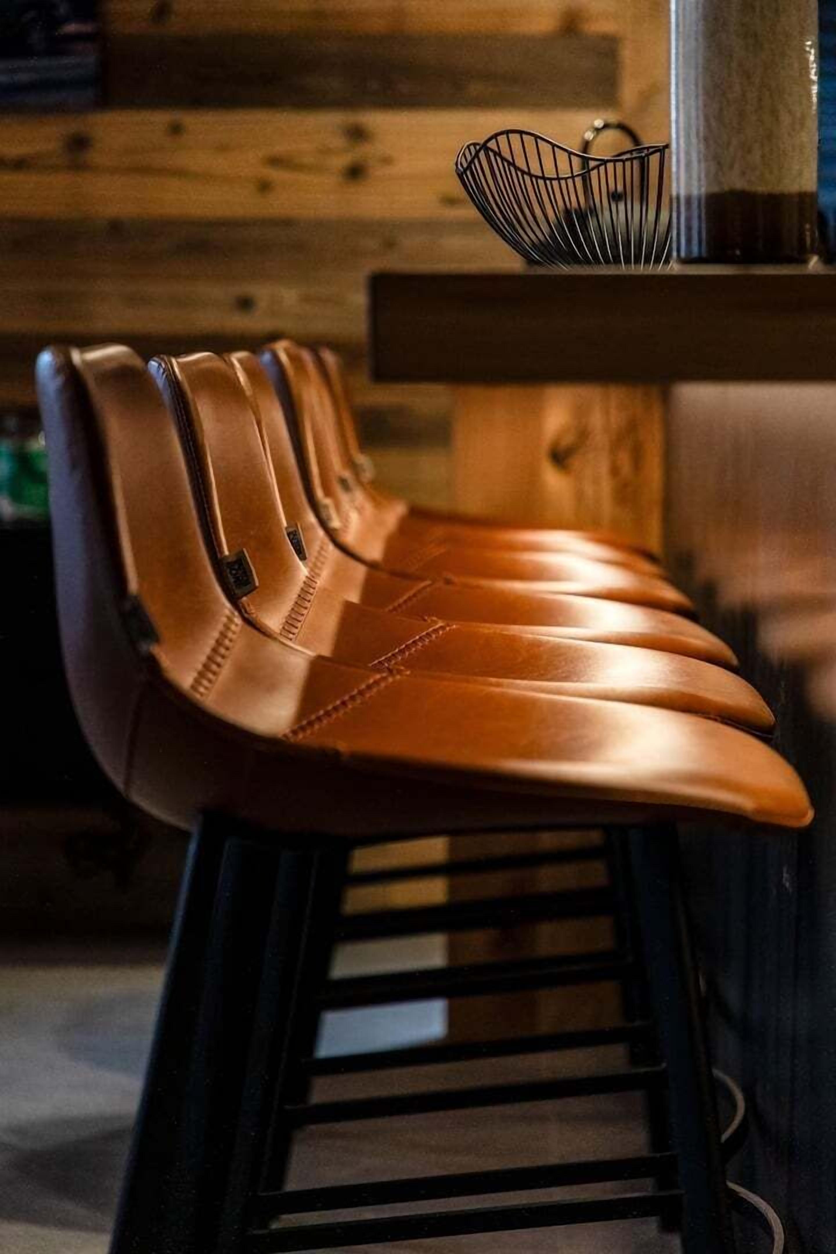 Une rangée de tabourets de bar en cuir marron, dotés de pieds en métal, est placée devant un mur en bois et un comptoir en métal.