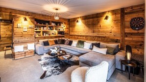 A cozy living room with a sectional sofa, a coffee table, and a fireplace. There are bookshelves and a dartboard on the walls. - PEARL 201 | LES GETS | 14 pers.  | Central (Les Gets)