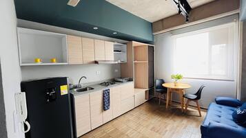 A compact kitchen with a refrigerator, stove, and sink, a dining area with a table and chairs, and a blue sofa.