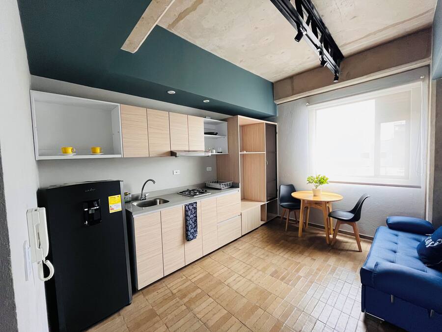 A compact kitchen with a refrigerator, stove, and sink, a dining area with a table and chairs, and a blue sofa.