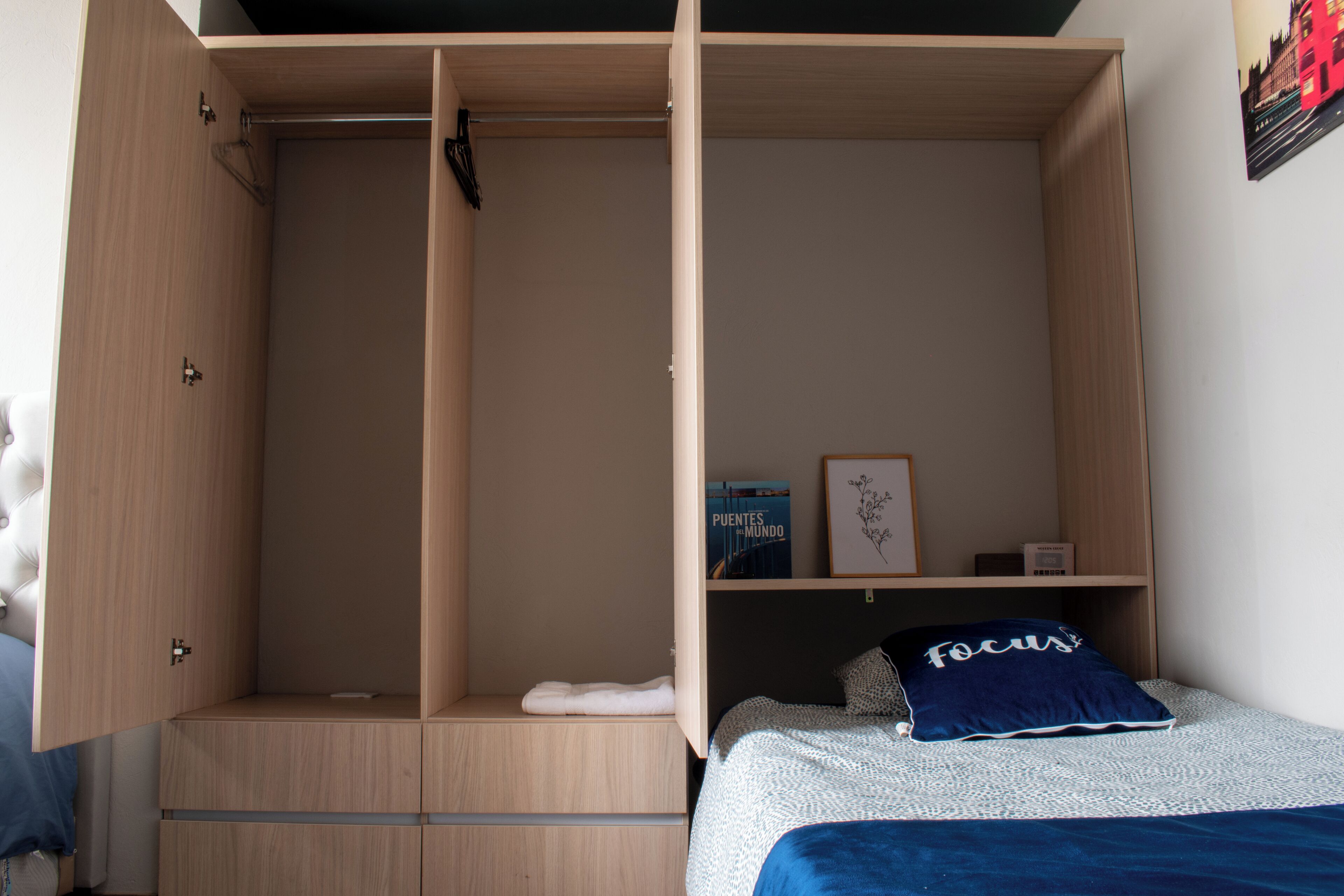 A bedroom with a bed, a wardrobe, and a shelf with books and a pillow.