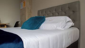 Una cama bien hecha con un cabecero capitonado, un plaid azul y una almohada blanca con diseño dorado.