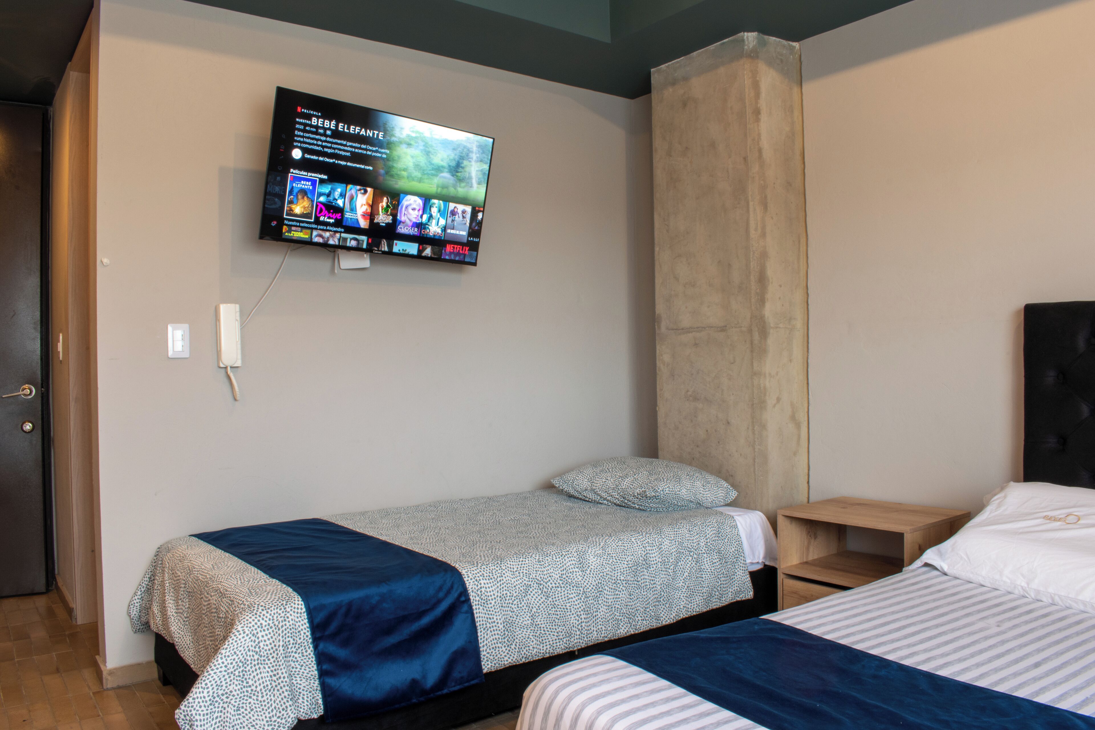 Un dormitorio con dos camas, un televisor montado en la pared y una mesita de noche de madera.
