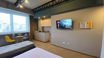 Une chambre d’hôtel moderne équipée d’un lit, d’une petite kitchenette, d’une télévision et d’un coin salon avec des fauteuils.