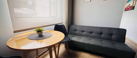 Ett modernt vardagsrum med en grå soffa, ett runt träbord med en växt och två inramade konstverk på väggen.