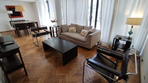 A living room with a sofa, coffee table, and a treadmill. There is a dining table with chairs and a lamp. - Recoleta tres dormitorios (Buenos Aires)