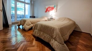 A room with two beds, a window with curtains, a nightstand with a lamp, and a painting on the wall. - Recoleta tres dormitorios (Buenos Aires)