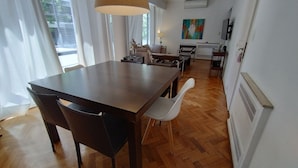 A dining area with a wooden table and chairs, a kitchen in the background, and a large window with curtains. - Recoleta tres dormitorios (Buenos Aires)
